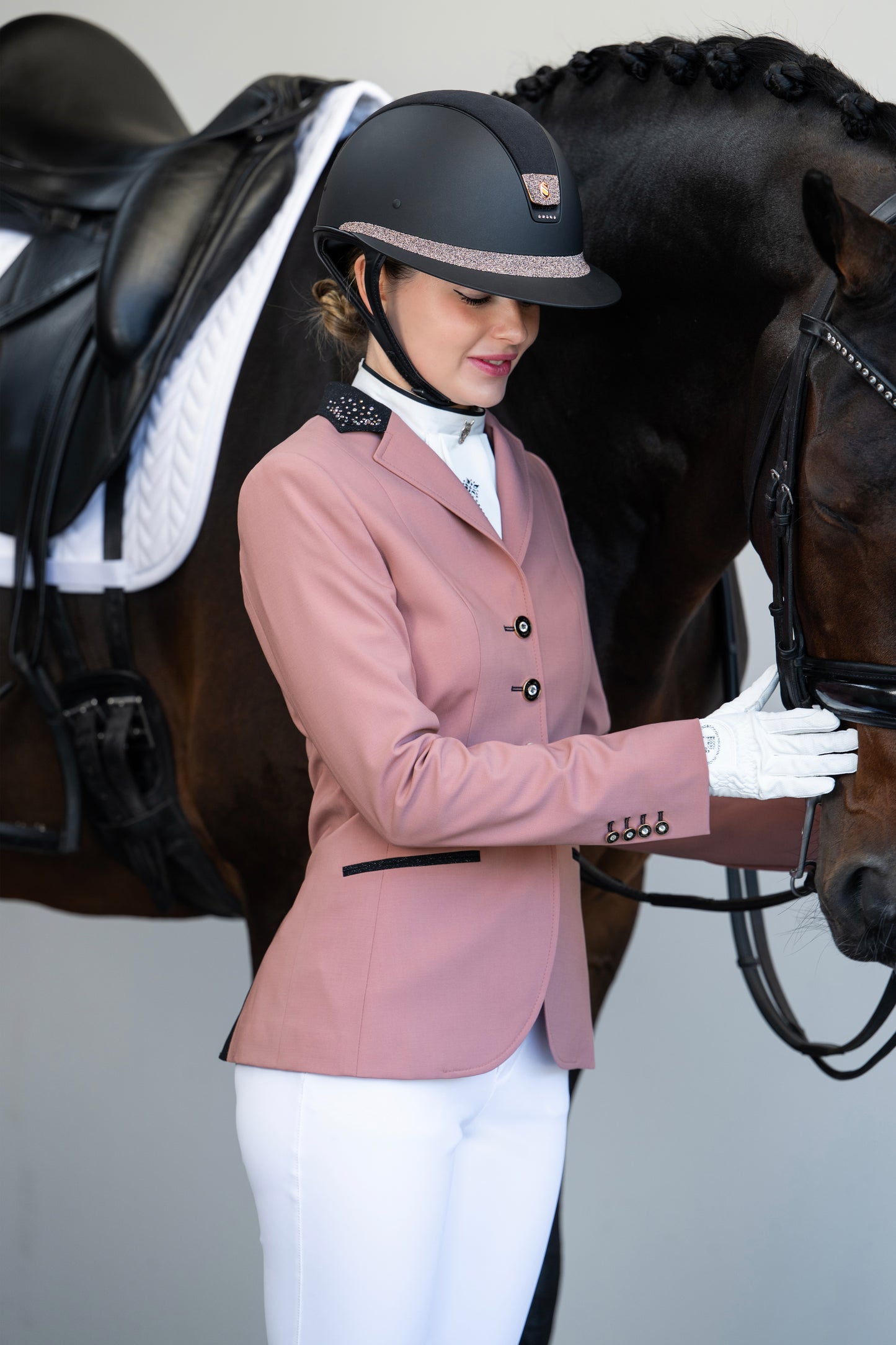 Model smiling and looking at her horse while holding the head wearing JuulC show coat in Blush Rose