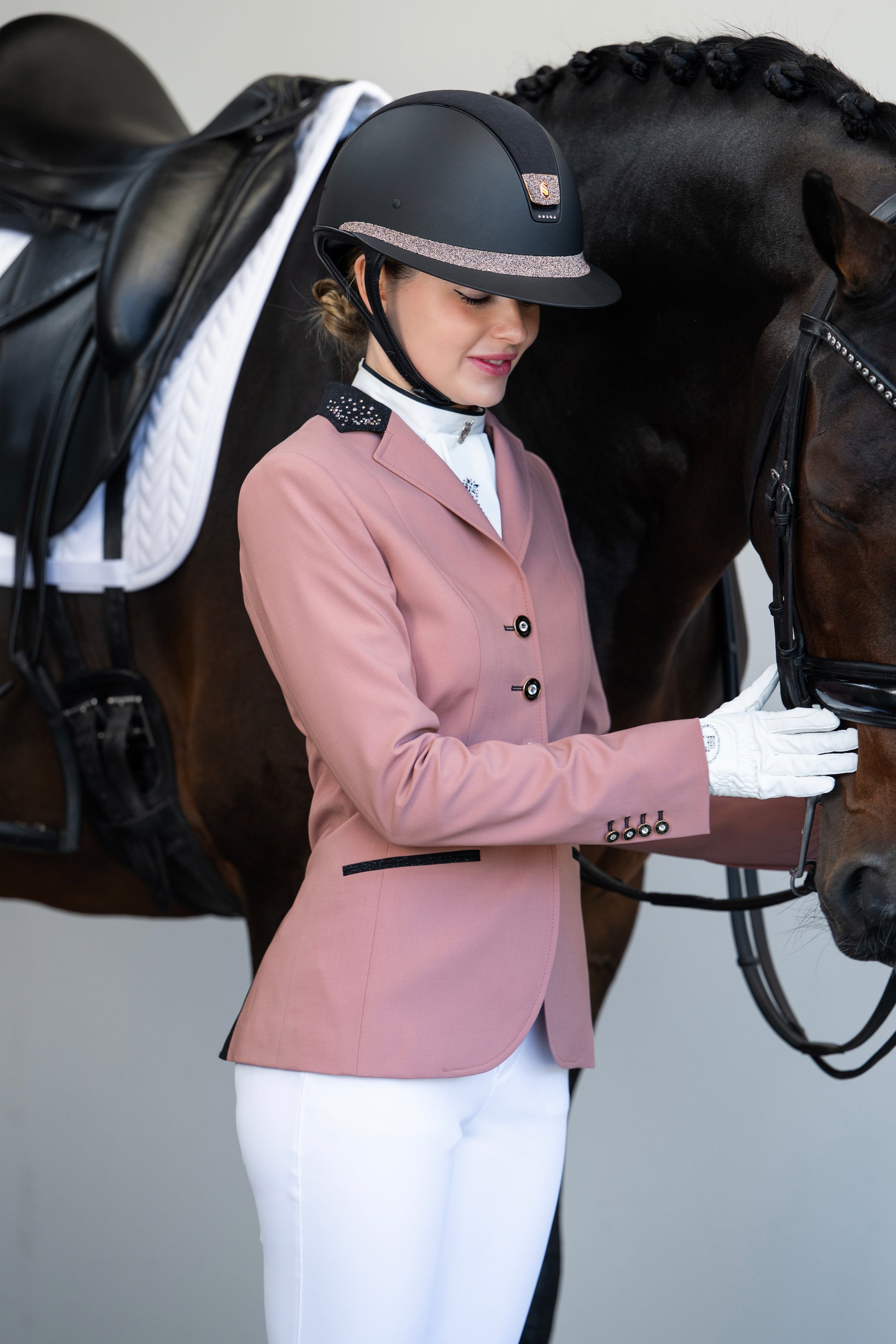 Model smiling and looking at her horse while holding the head wearing JuulC show coat in Blush Rose