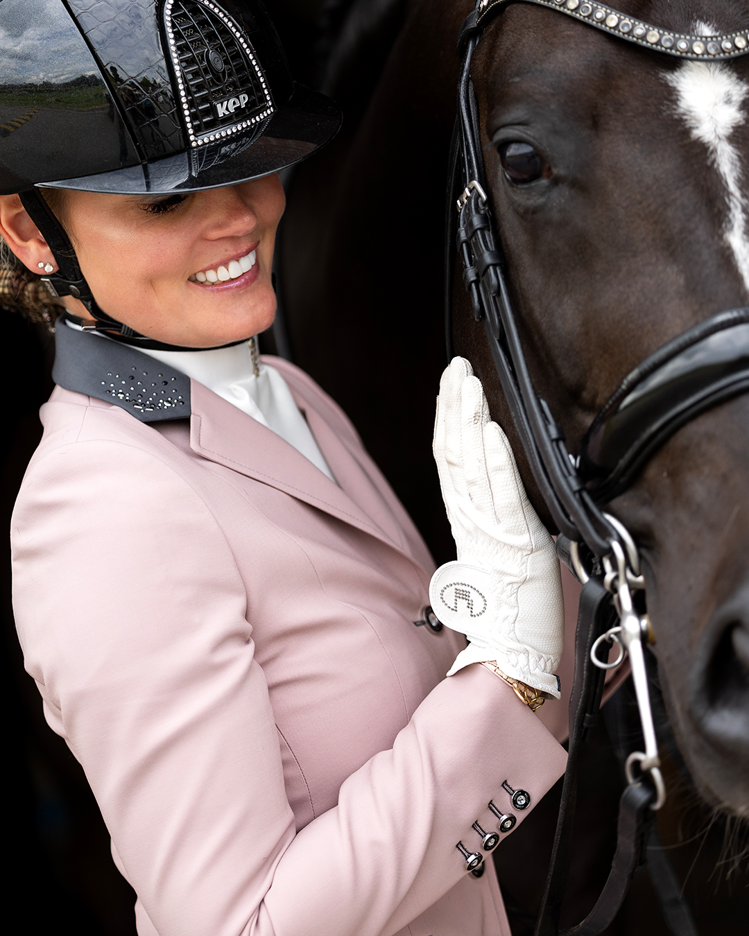 Model smiling while holding her horse and showing the side of JuulC' Powder Pink  Show Coat for women